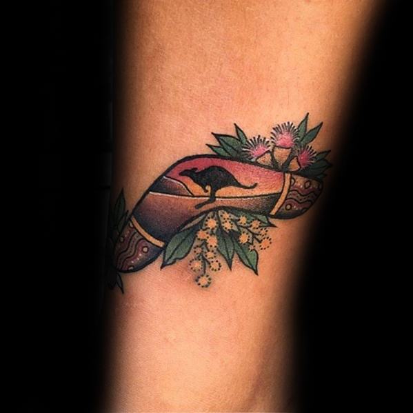 Boomerang tattoo with an Australian sunset scene, kangaroo silhouette, and native flowers surrounding the design.