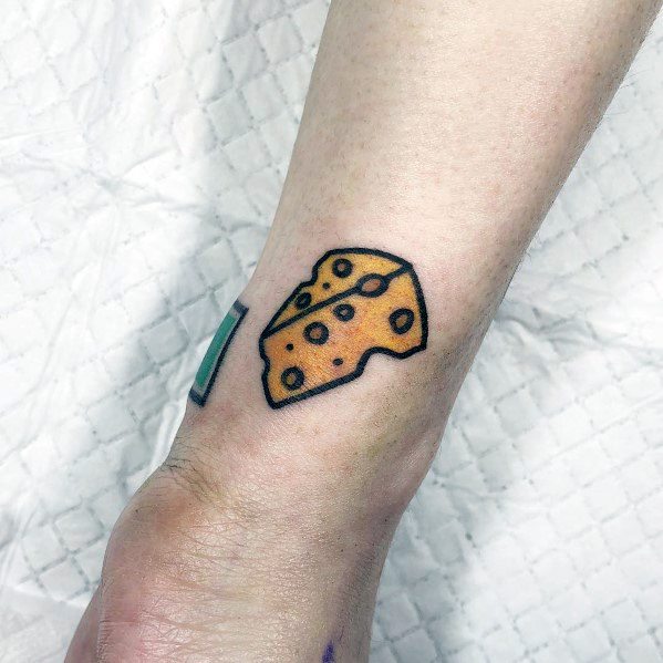 Minimalist cheese tattoo on the wrist, featuring a small wedge of Swiss cheese with bold black outlines and simple yellow-orange shading.
