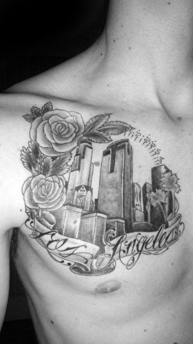 Chest tattoo of Los Angeles skyline with roses and script lettering that reads "Los Angeles" in black and gray ink.
