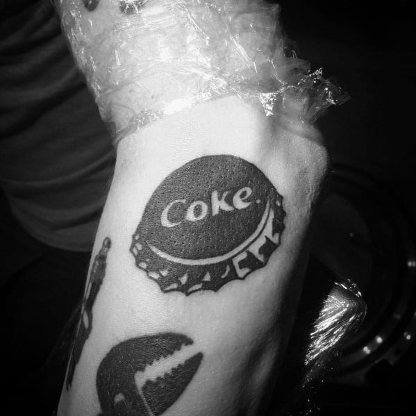 Black and white Coca-Cola bottle cap tattoo with bold shading and crisp details, creating a vintage and nostalgic design on the wrist.