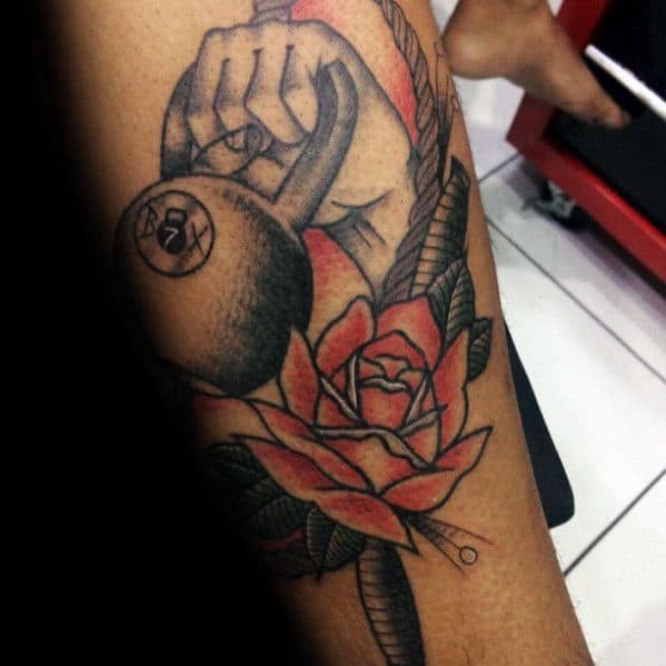 Bold kettlebell tattoo featuring a hand gripping a rope, accented with a red rose, symbolizing strength, resilience, and passion for fitness.
