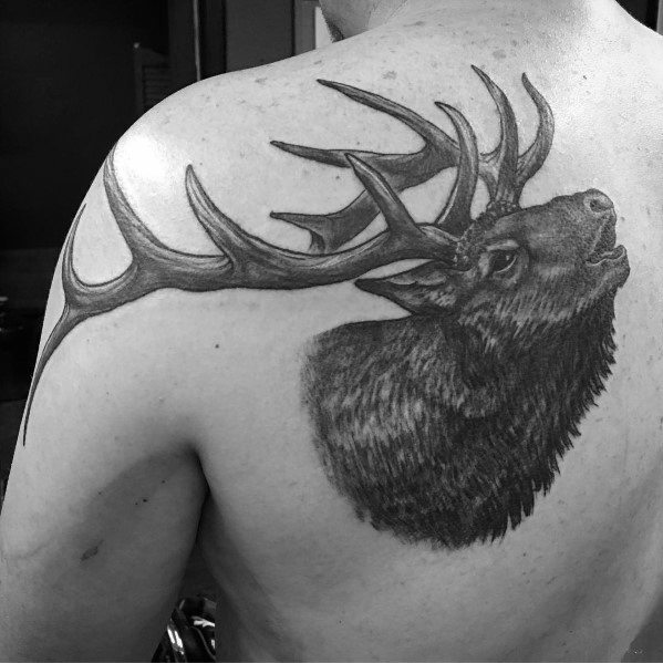 Realistic black and grey elk tattoo on the upper back and shoulder, featuring detailed shading and bold antlers for a striking design.
