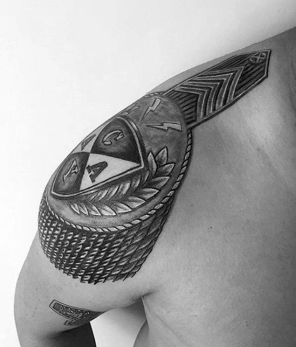Epaulette tattoo with tribal-style patterns, sharp geometric symbols, and textured tassels wrapping over the upper shoulder.