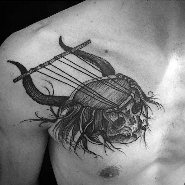Tattoo of a skull with flowing hair, fused with a horned lyre-like instrument, blending music and death symbolism across the chest.