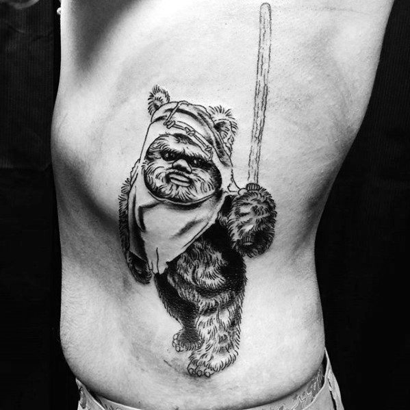 Black and white Ewok tattoo on the ribs, featuring a detailed fur texture, raised spear, and confident stance in a sketch-like style.