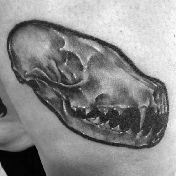 Realistic black and grey fox skull tattoo on the upper arm, featuring smooth shading and defined bone structure.