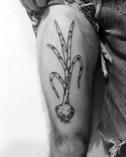 Black and grey garlic tattoo on the thigh with fine linework and shading, featuring long, curved stems for a bold botanical design.