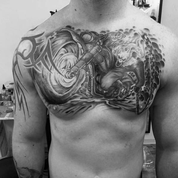Black and grey Ghost Rider chest tattoo with flaming skull, motorcycle, swirling smoke, and large chain stretching across the shoulder.