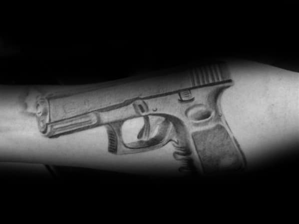 Black and grey tattoo of a Glock pistol on the forearm, featuring soft shading and fine details for a realistic and three-dimensional effect.