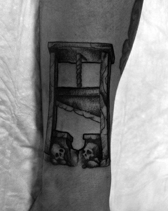 Black and grey guillotine tattoo with cracked stone frame, shaded blade, and skulls beneath the structure for a grim aesthetic.