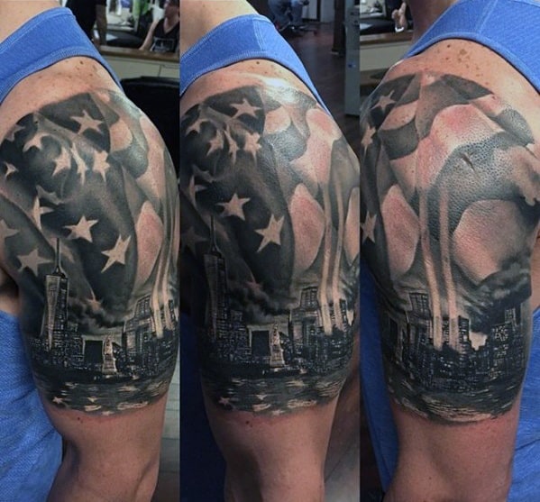 Patriotic upper arm tattoo featuring the New York City skyline with the Twin Towers and a large American flag waving above.