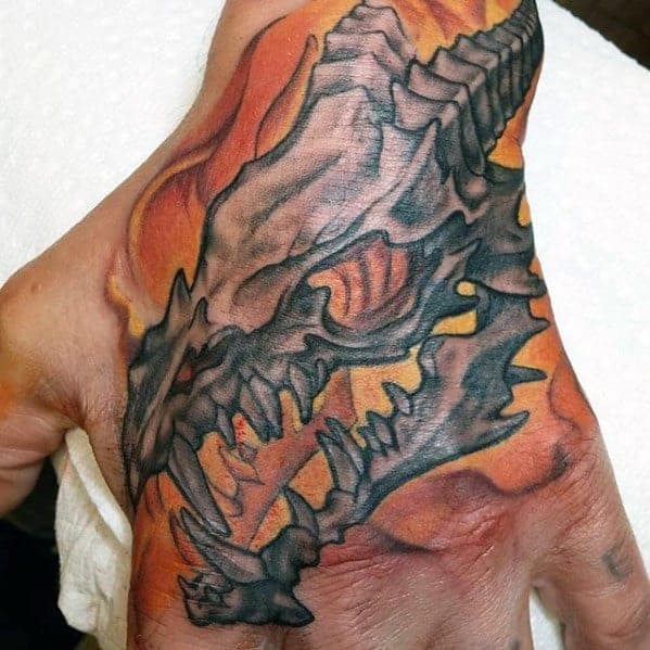 A hand tattoo featuring a dragon skull with a fiery background