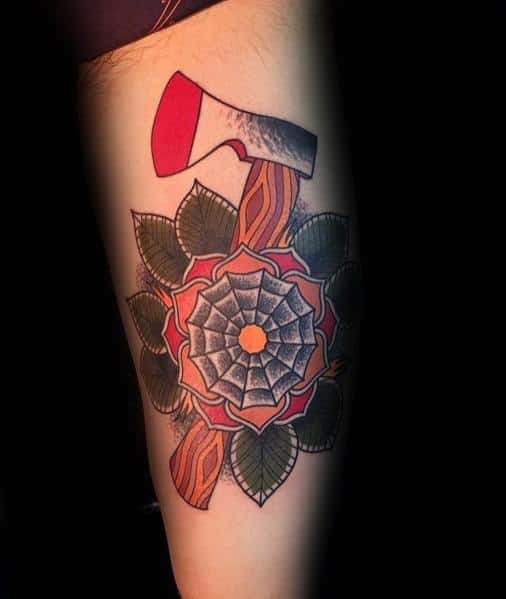 Hatchet tattoo with a red-tipped blade and wooden handle, set against a bold geometric flower with intricate petals and green leaves.