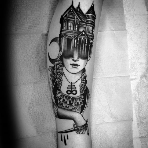 Forearm tattoo of a Victorian woman with a haunted house replacing her eyes, crescent moon beside her, and gothic necklace detail.