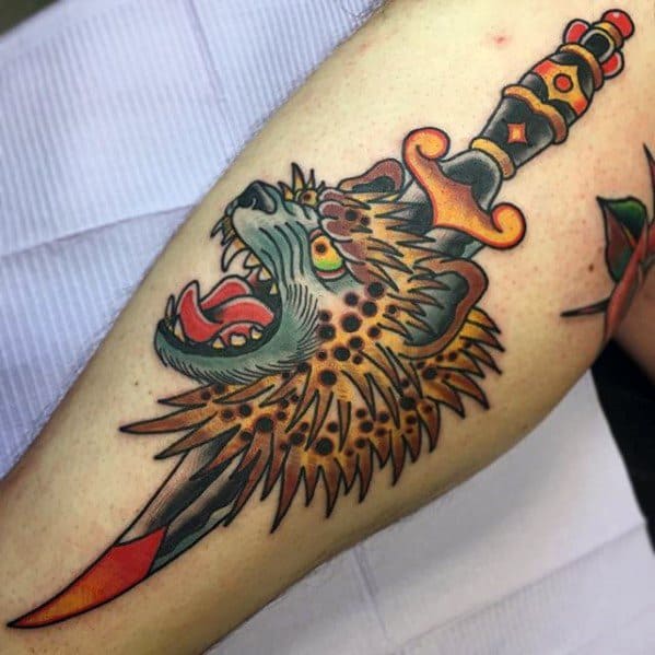 Traditional-style hyena tattoo on the leg, featuring a dagger piercing through its head with bold outlines and vibrant red, orange, and green tones.