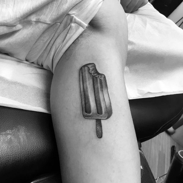 Black and grey tattoo of a bitten popsicle on the inner arm, featuring smooth shading and fine details for a realistic look.
