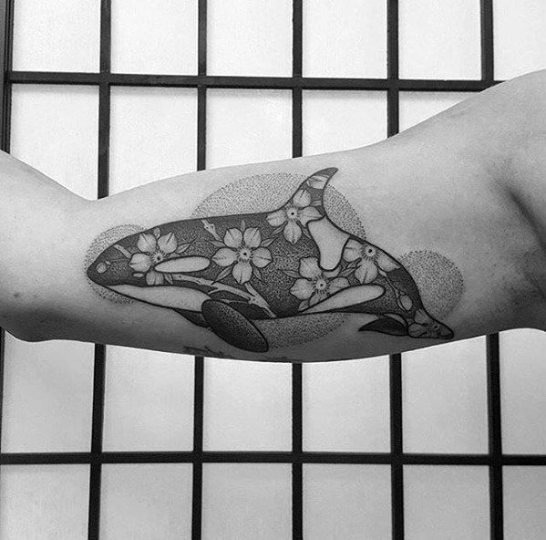 Black and gray orca tattoo on the forearm, adorned with dotwork shading and floral details, blending nature and elegance in the whale's design.