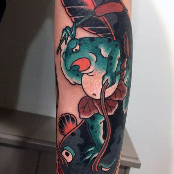 Japanese-style forearm tattoo featuring a fierce green frog gripping a branch, with a koi fish and lotus leaves in a bold traditional design.