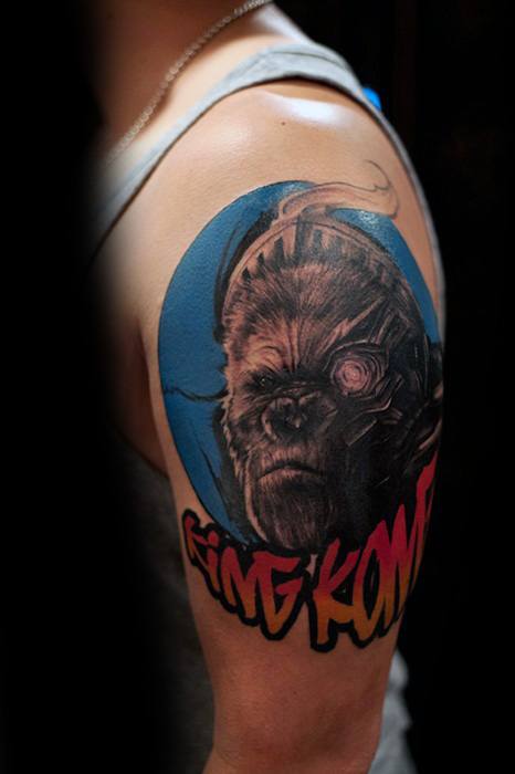 Colorful cyborg King Kong tattoo on upper arm with a blue background and bold red-yellow “King Kong” text in graffiti style.