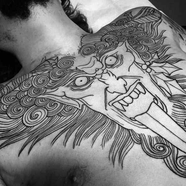 Large black linework Krampus tattoo covering the chest, featuring intense eyes, swirling hair, fangs, and a dramatic tongue.