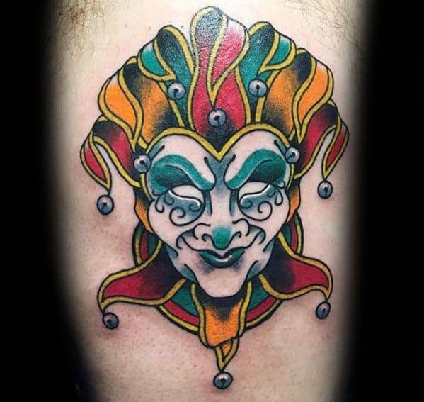 A colorful tattoo of a jester's face with vibrant red, yellow, and green colors, adorned with bells on the hat, capturing a playful yet bold expression.