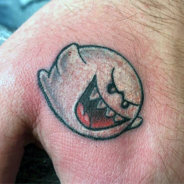 Mario ghost tattoo featuring Boo with an aggressive grin, bold black outline, and grey shading, inked on the hand for a striking look.