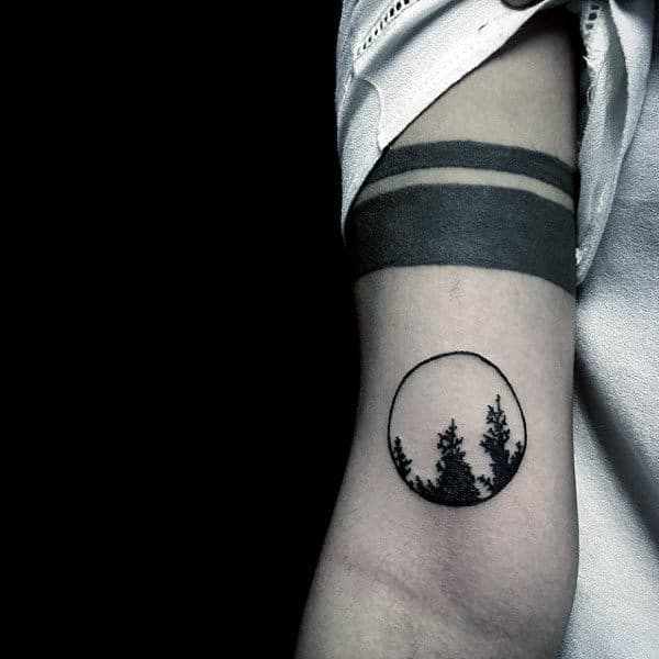 Tattoo of pine trees in a circle on an arm, with two black bands above it