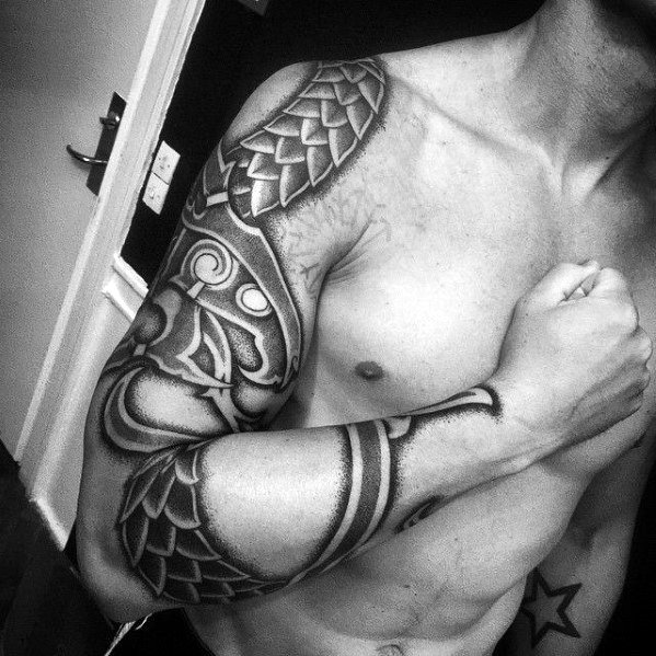 Viking-inspired blackwork sleeve tattoo with bold patterns, dragon scales, and Norse ornamental elements wrapping the shoulder and arm.