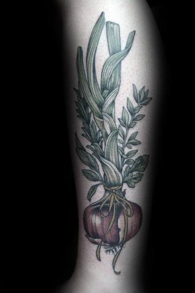 Realistic onion tattoo on the forearm with fine details, featuring long green leaves, delicate roots, and surrounding botanical elements.