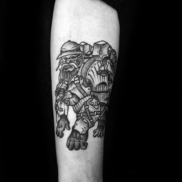 Black and grey tattoo of Torbjörn from Overwatch in his armored suit, detailed with mechanical gear on a man's forearm.