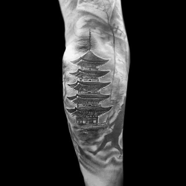 Black and grey tattoo of a traditional Japanese pagoda with misty mountain-like shading and soft background textures on the forearm.