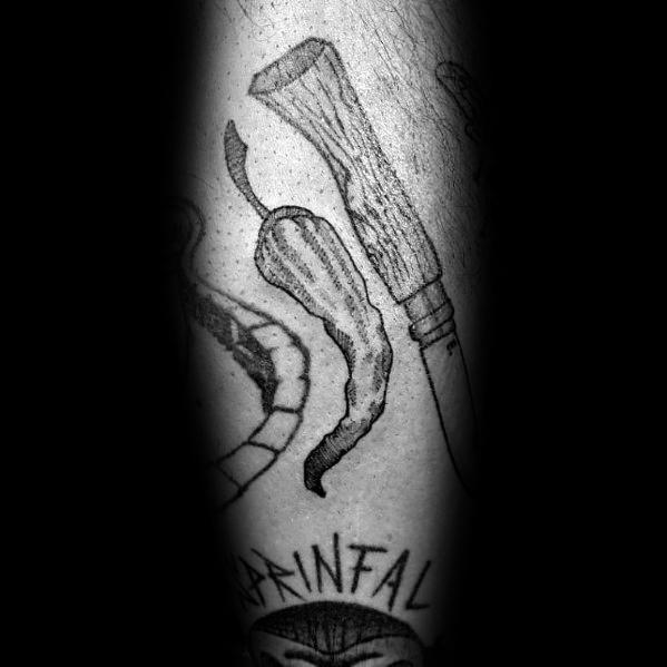 Black and grey chili pepper tattoo with a rustic, hand-drawn style, placed alongside a knife for a bold and edgy look.