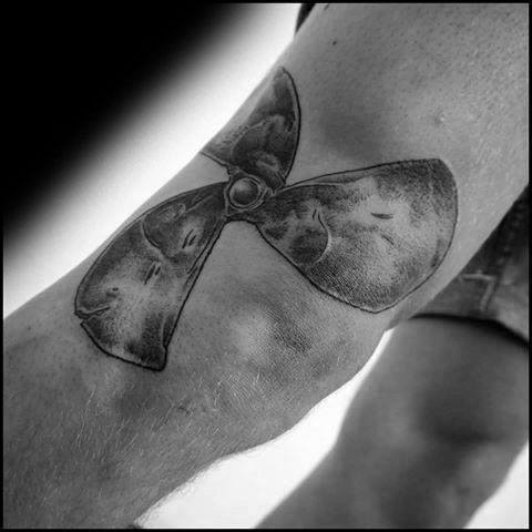 Black and grey tattoo of a three-blade propeller on the elbow, with shading and texture for a worn, industrial look.