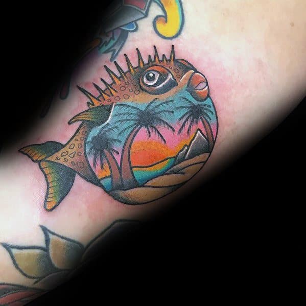 Colorful pufferfish tattoo with a tropical sunset scene inside its body, blending marine life with vibrant beach-inspired artistry.