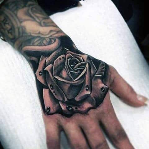 Tattoo of a realistic rose with water droplets on a hand
