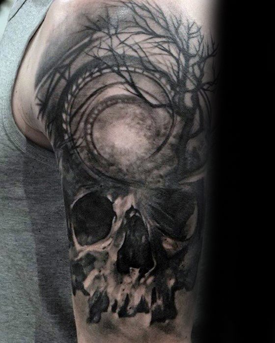 Dark roller coaster tattoo on upper arm featuring a skull, eerie trees, and track circling a full moon in a haunting night scene.