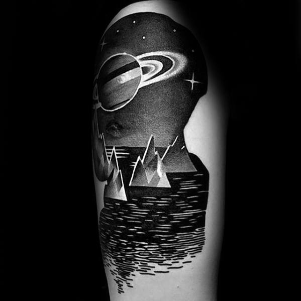 Bold black Saturn tattoo design for men featuring sharp mountains, a reflective lake, and a surreal cosmic sky.