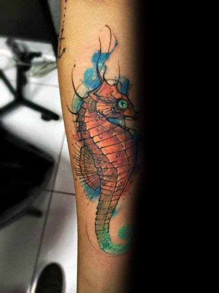 Watercolor seahorse tattoo on forearm, featuring vibrant orange and blue hues with a soft, artistic splash effect for a fluid, dynamic look.