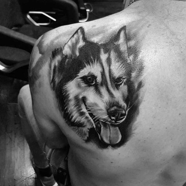 Realistic Siberian Husky tattoo on a man's upper back, featuring detailed fur shading and a happy expression for a lifelike and dynamic design.
