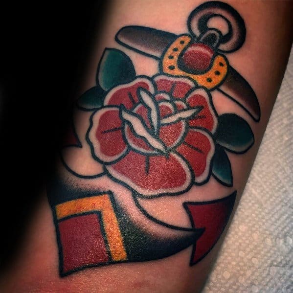 Classic anchor and rose tattoo in bold traditional style, featuring black outlines, red shading, and green leaves for a timeless look.