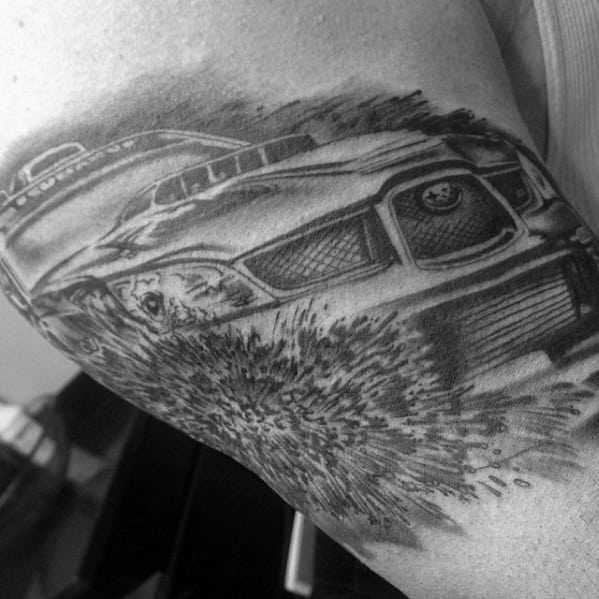 Black and grey Subaru rally car tattoo on the upper arm, showcasing a dynamic scene with the car kicking up dirt and debris in motion.