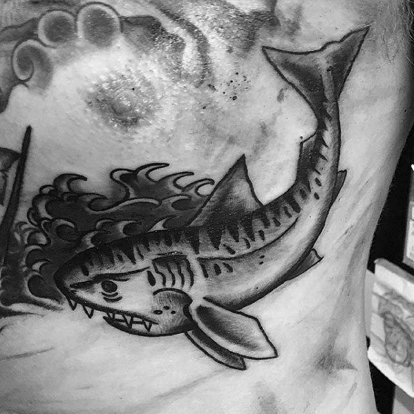 Black and grey tiger shark tattoo with bold shading, stylized waves, and classic old-school design on the side of the torso.