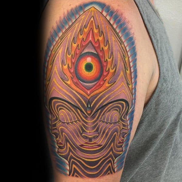 Vibrant Tool-inspired upper arm tattoo featuring a psychedelic face with flame-like lines and a glowing third eye at the top.