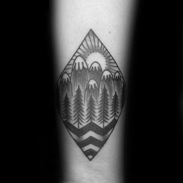 Geometric blackwork tattoo featuring pine trees, snowy mountains, a rising sun, and bold chevron lines in a diamond frame.