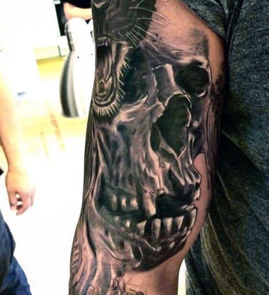 Black and grey tattoo sleeve featuring a detailed skull merging with a roaring animal, creating a dark and intense design on the arm