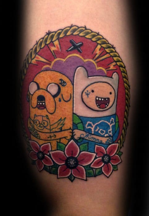 Traditional-style Adventure Time tattoo of Jake and Finn holding portraits of each other, framed with flowers and rope detailing on the arm.