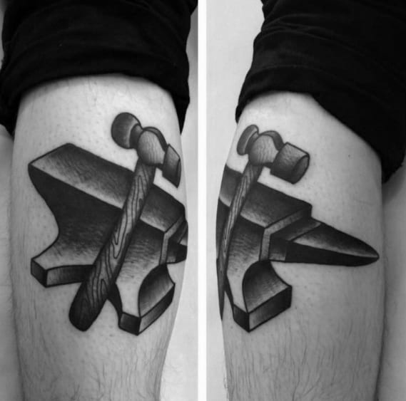 Black and grey anvil tattoo split across both thighs, featuring a detailed hammer with woodgrain texture resting diagonally on the anvil.