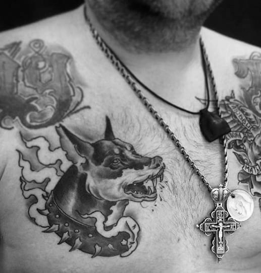 Aggressive Doberman chest tattoo with a spiked collar and flame-like elements, done in bold black and grey for a powerful impact.