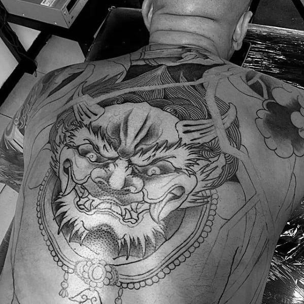 Black and grey Raijin back tattoo with fierce facial expression, bold outlines, and traditional Japanese detailing in progress.