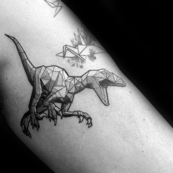 Geometric velociraptor tattoo with angular shapes and shaded facets, paired with origami-style birds for a unique and creative design.